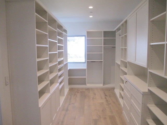 Large beach style gender-neutral walk-in wardrobe in Los Angeles with shaker cabinets, white cabinets and light hardwood floors.