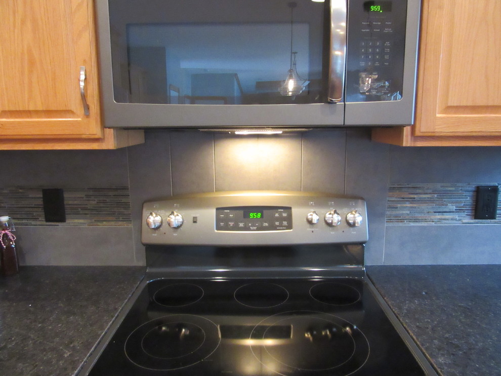 Transitional u-shaped light wood floor eat-in kitchen photo with an undermount sink, raised-panel cabinets, medium tone wood cabinets, granite countertops, gray backsplash, ceramic backsplash, black appliances and two islands