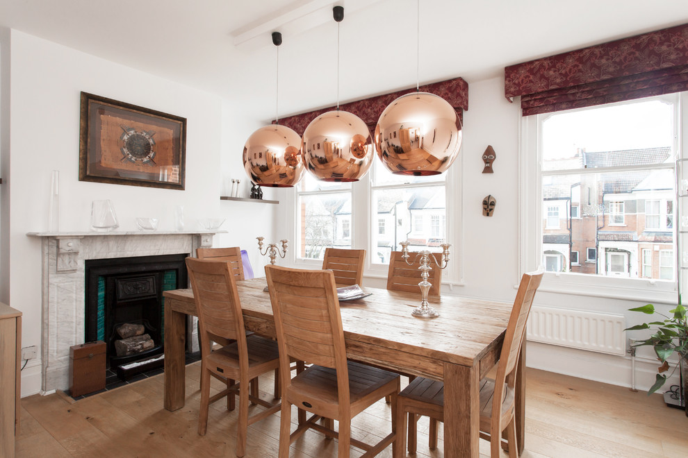 This is an example of a scandinavian dining room in London with white walls, medium hardwood floors and a standard fireplace.
