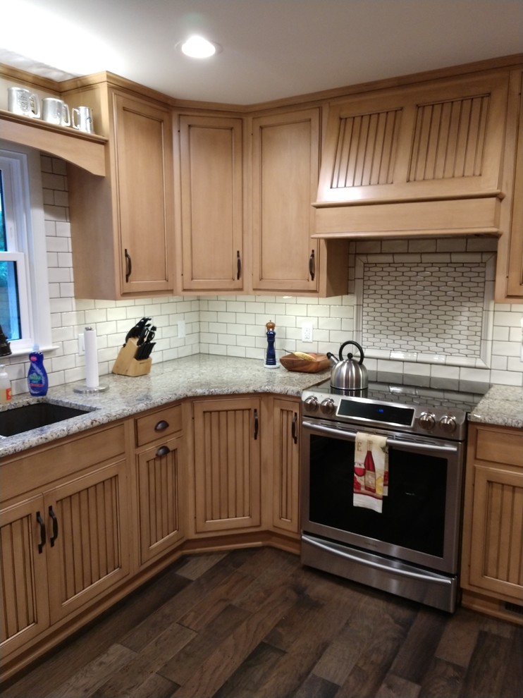 Mid-sized mountain style laminate floor and multicolored floor home design photo with distressed cabinets, granite countertops, white backsplash, subway tile backsplash, stainless steel appliances, no island and multicolored countertops