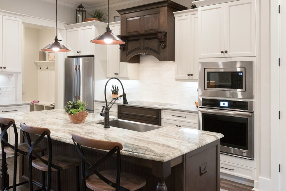 Photo of a mid-sized country l-shaped kitchen in Atlanta with a farmhouse sink, recessed-panel cabinets, white cabinets, white splashback, subway tile splashback, stainless steel appliances, dark hardwood floors, with island and brown floor.