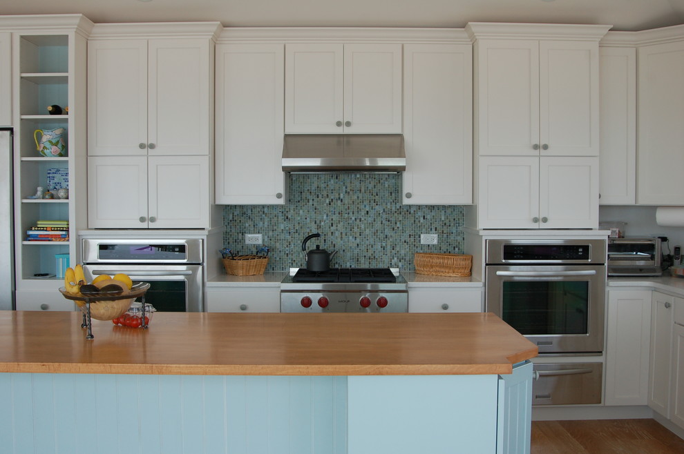 Photo of a beach style eat-in kitchen in Boston with a farmhouse sink, recessed-panel cabinets, blue cabinets, wood benchtops, multi-coloured splashback, stainless steel appliances, medium hardwood floors and with island.