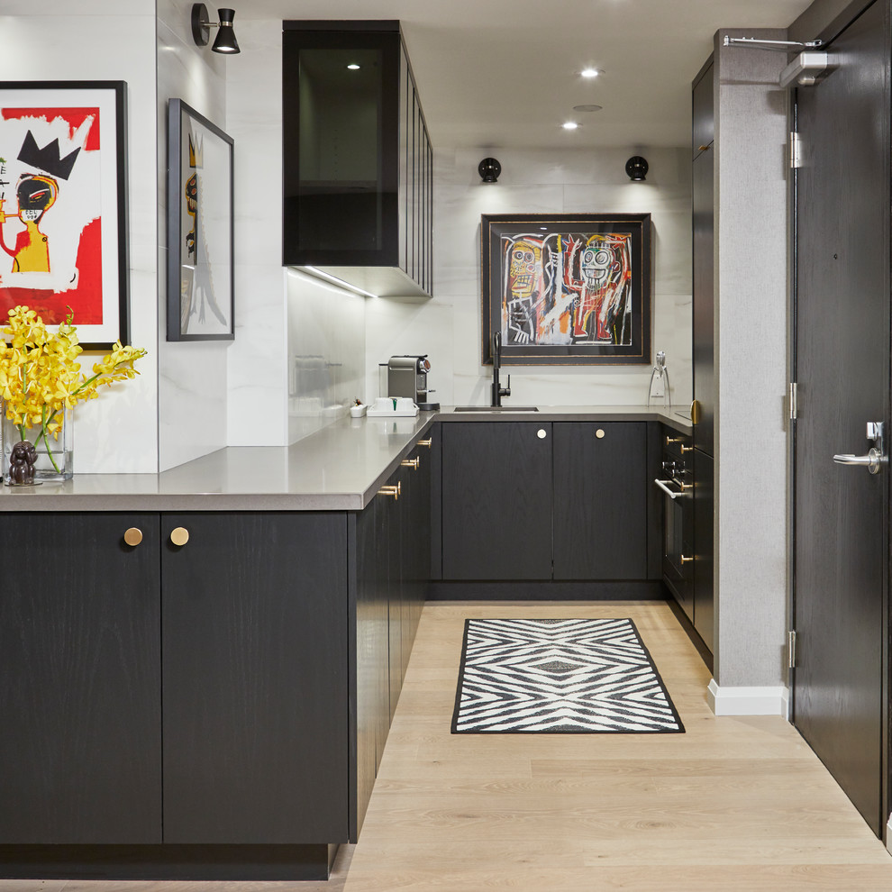 This is an example of a small contemporary u-shaped eat-in kitchen in Toronto with flat-panel cabinets, black cabinets, quartz benchtops, white splashback, porcelain splashback, panelled appliances, light hardwood floors, no island, grey benchtop, an undermount sink and beige floor.