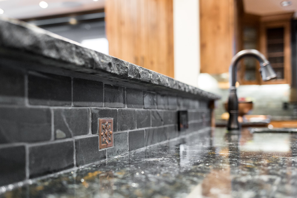 Mountain style galley medium tone wood floor eat-in kitchen photo in Vancouver with a farmhouse sink, beaded inset cabinets, medium tone wood cabinets, solid surface countertops, gray backsplash, stone tile backsplash, stainless steel appliances and an island