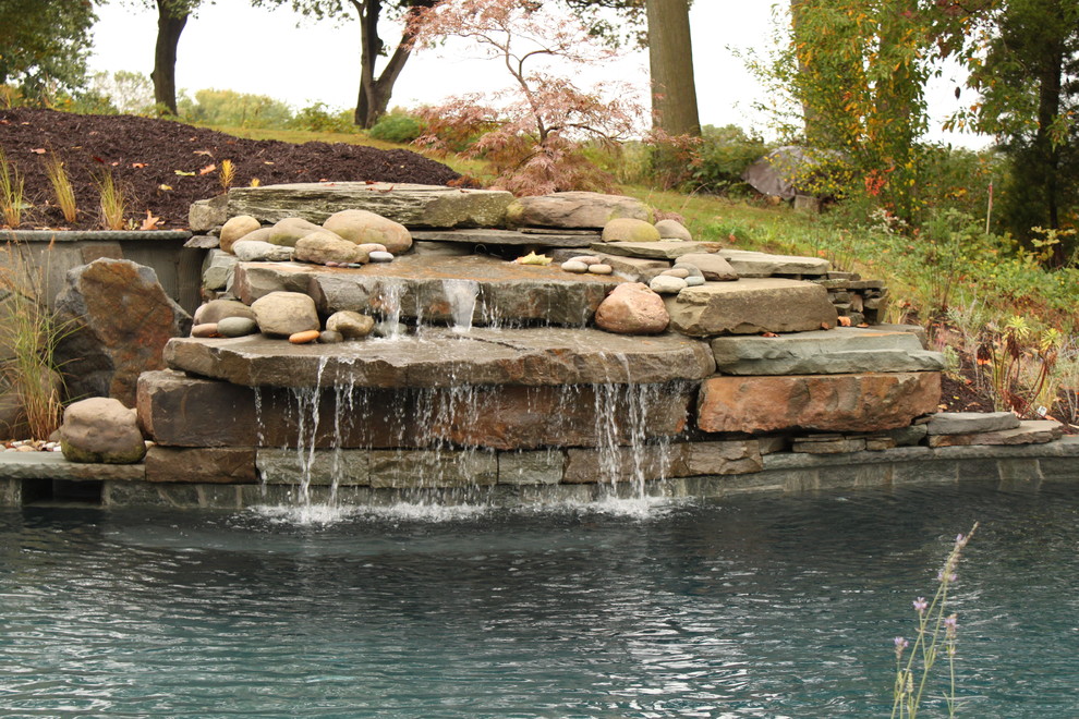 Photo of a mid-sized traditional backyard custom-shaped infinity pool in Baltimore with natural stone pavers and a water feature.