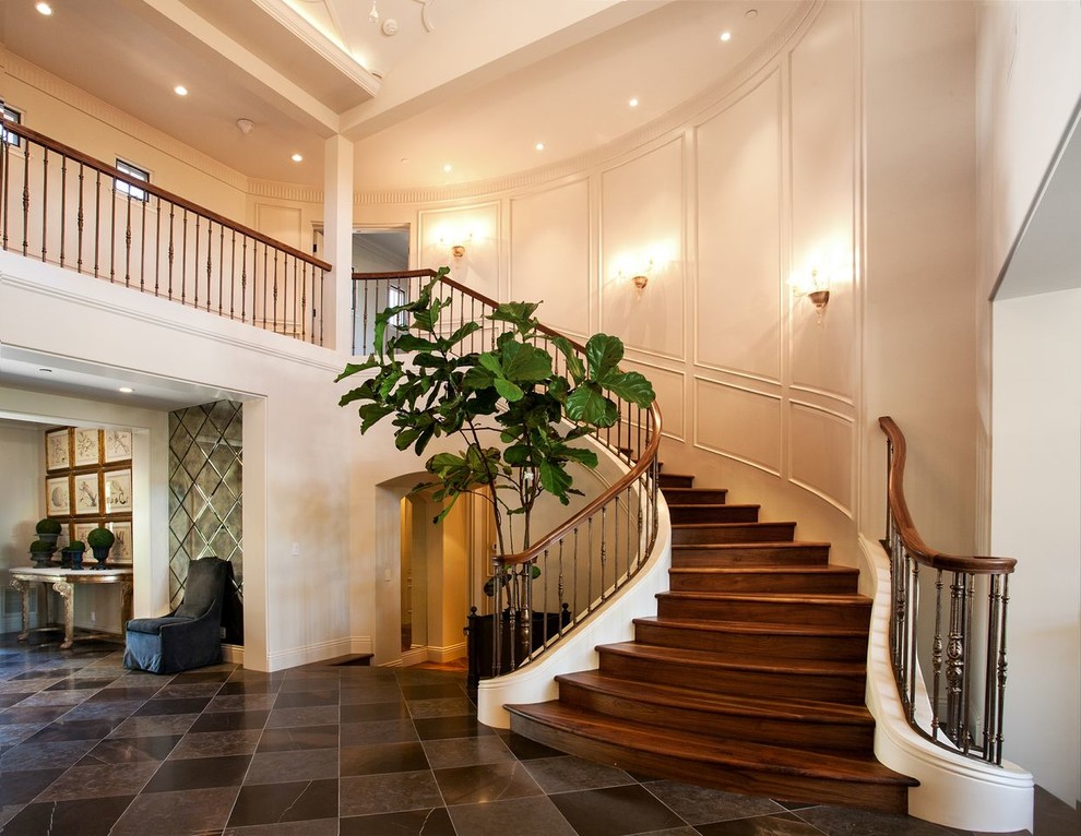 This is an example of a large mediterranean wood curved staircase in Orange County with wood risers and mixed railing.