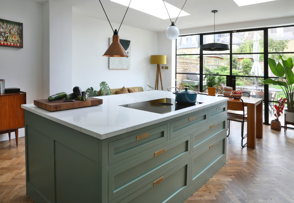 Inspiration for a medium sized classic l-shaped kitchen/diner in London with an integrated sink, shaker cabinets, green cabinets, quartz worktops, white splashback, engineered quartz splashback, stainless steel appliances, medium hardwood flooring, an island, brown floors and white worktops.