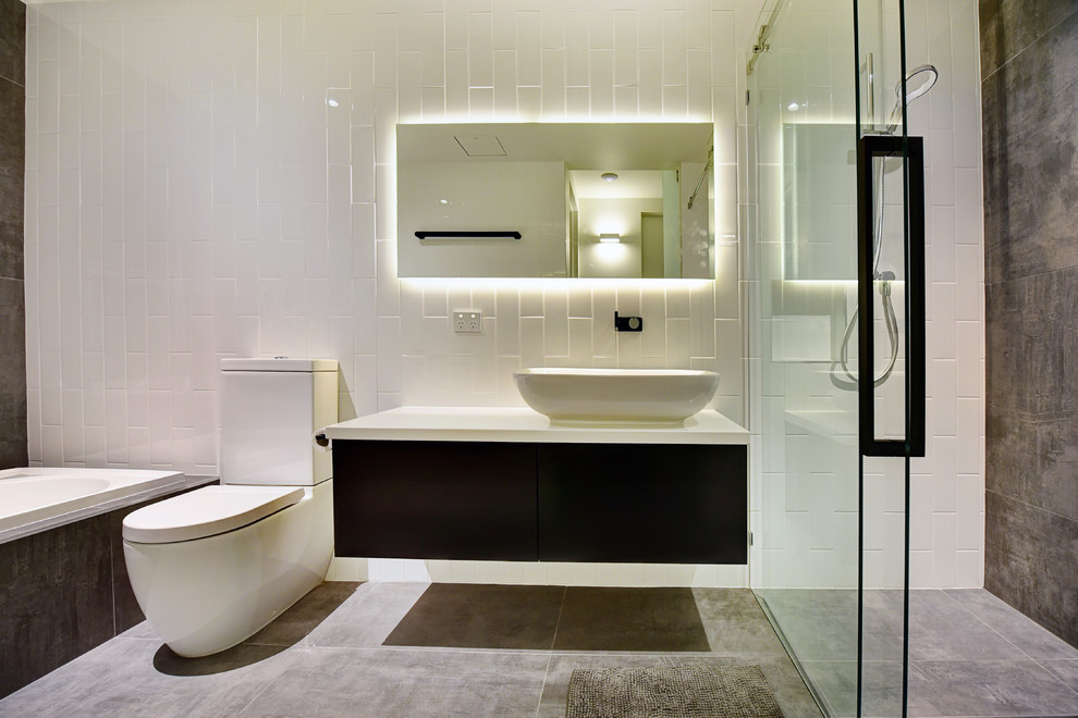 Photo of a contemporary 3/4 bathroom in Other with flat-panel cabinets, black cabinets, a drop-in tub, a curbless shower, gray tile, white tile, subway tile, a vessel sink, grey floor and a sliding shower screen.