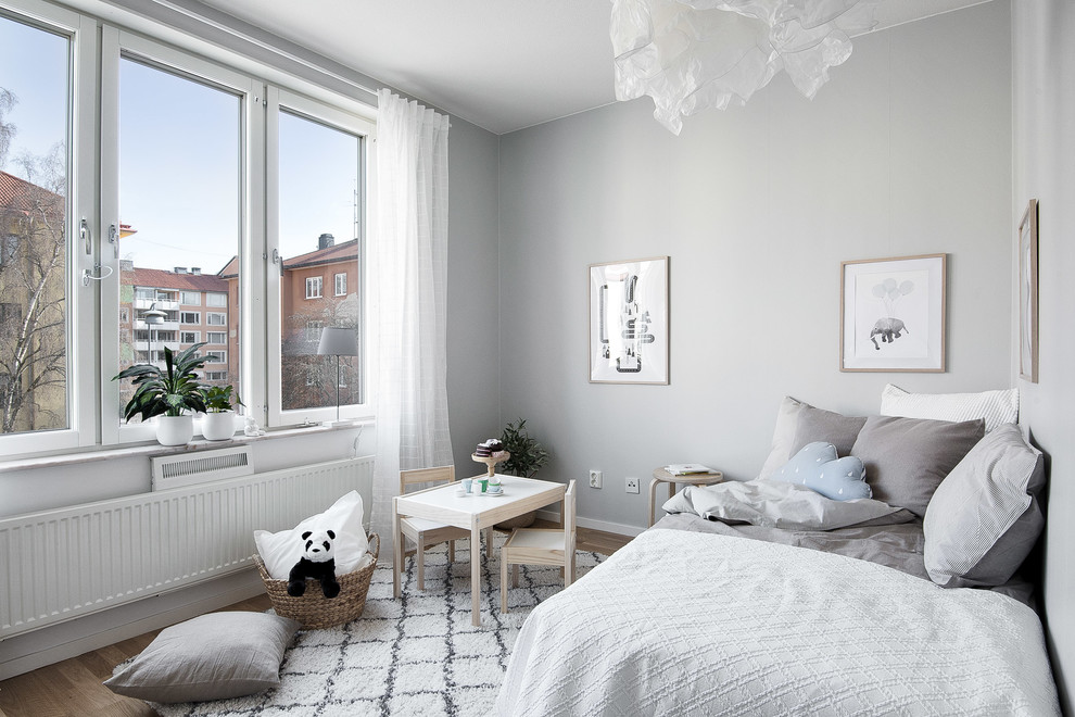 Photo of a scandinavian gender-neutral kids' bedroom in Stockholm with grey walls, medium hardwood floors and brown floor.