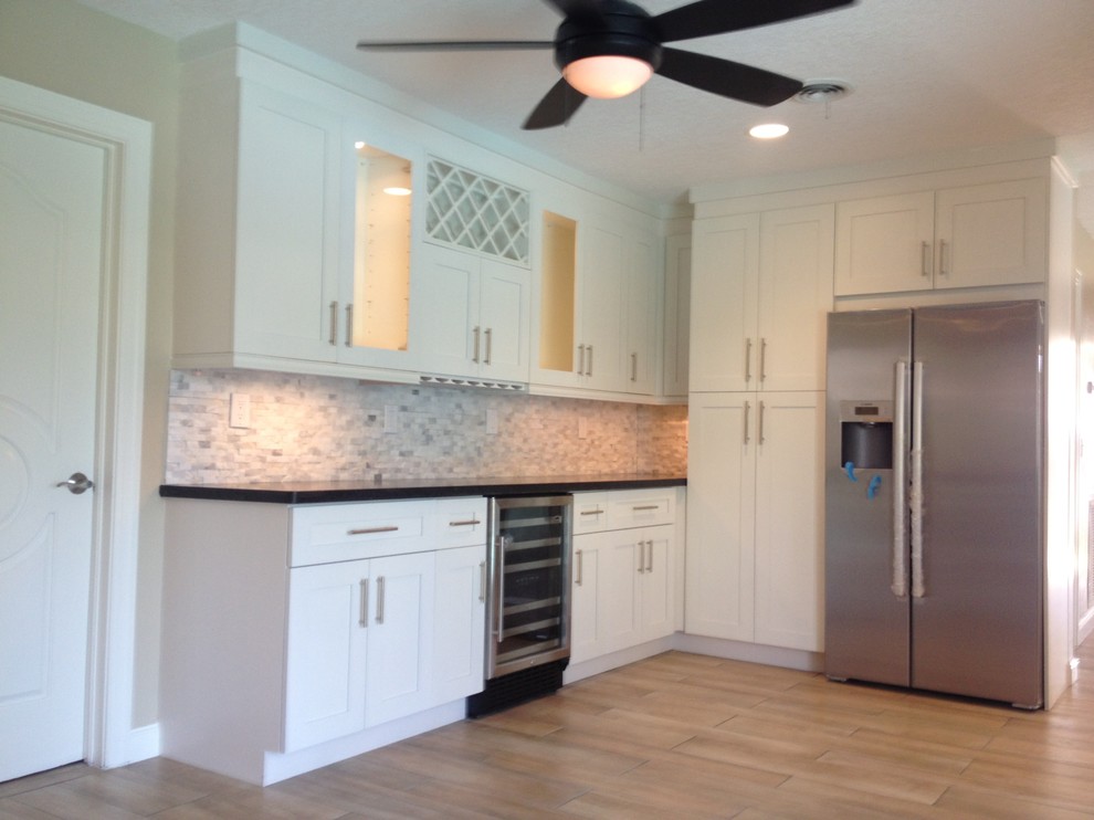 Open concept kitchen - small transitional l-shaped light wood floor and beige floor open concept kitchen idea in Miami with shaker cabinets, white cabinets, solid surface countertops, multicolored backsplash, stone tile backsplash and stainless steel appliances