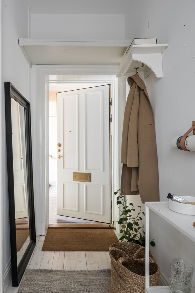 Mid-sized scandinavian entryway in Stockholm with white walls and light hardwood floors.