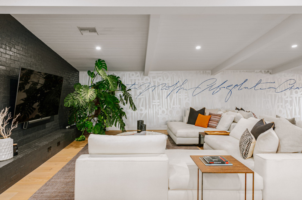 This is an example of an expansive midcentury open concept family room in Los Angeles with multi-coloured walls, light hardwood floors, a brick fireplace surround, a wall-mounted tv and beige floor.