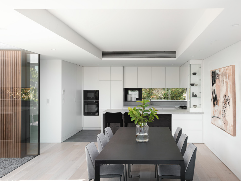 This is an example of a mid-sized modern u-shaped eat-in kitchen in Sydney with flat-panel cabinets, white cabinets, quartz benchtops, grey splashback, engineered quartz splashback, black appliances, ceramic floors, grey floor, grey benchtop, a peninsula and recessed.