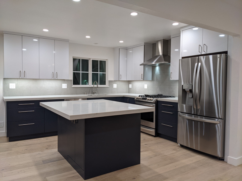 Bild på ett mellanstort funkis vit vitt kök, med en undermonterad diskho, släta luckor, blå skåp, bänkskiva i kvarts, grått stänkskydd, rostfria vitvaror, mellanmörkt trägolv, en köksö och beiget golv
