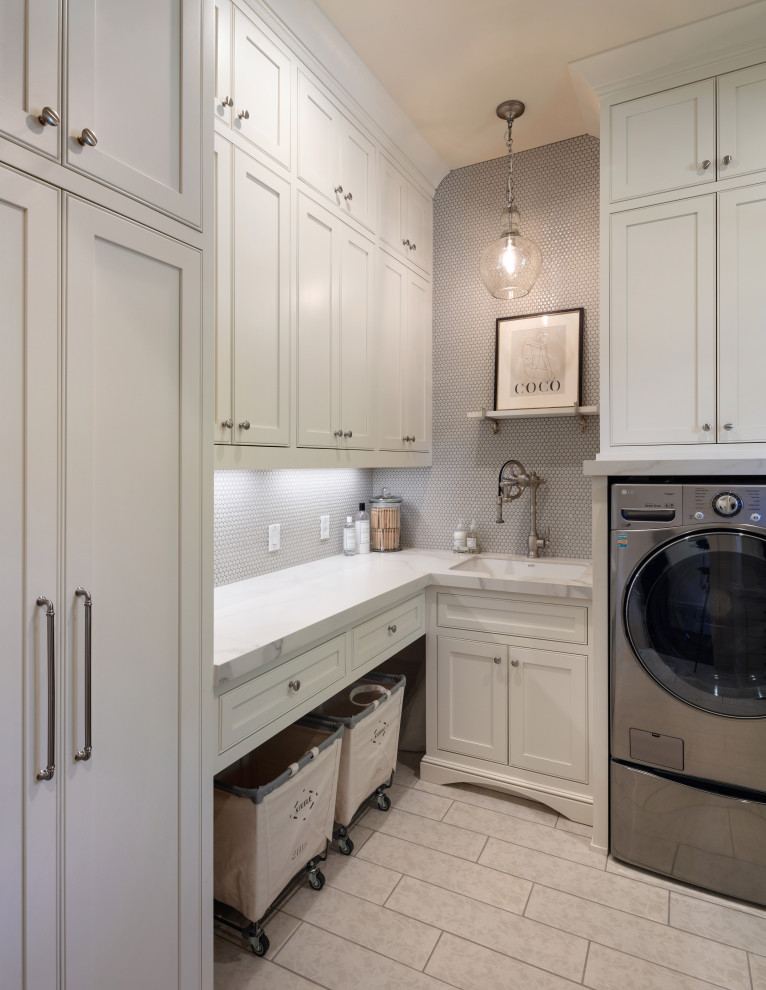 Mid-sized transitional dedicated laundry room in Atlanta with an undermount sink, beaded inset cabinets, white cabinets, solid surface benchtops, mosaic tile splashback, grey walls, porcelain floors, a side-by-side washer and dryer, grey floor and white benchtop.