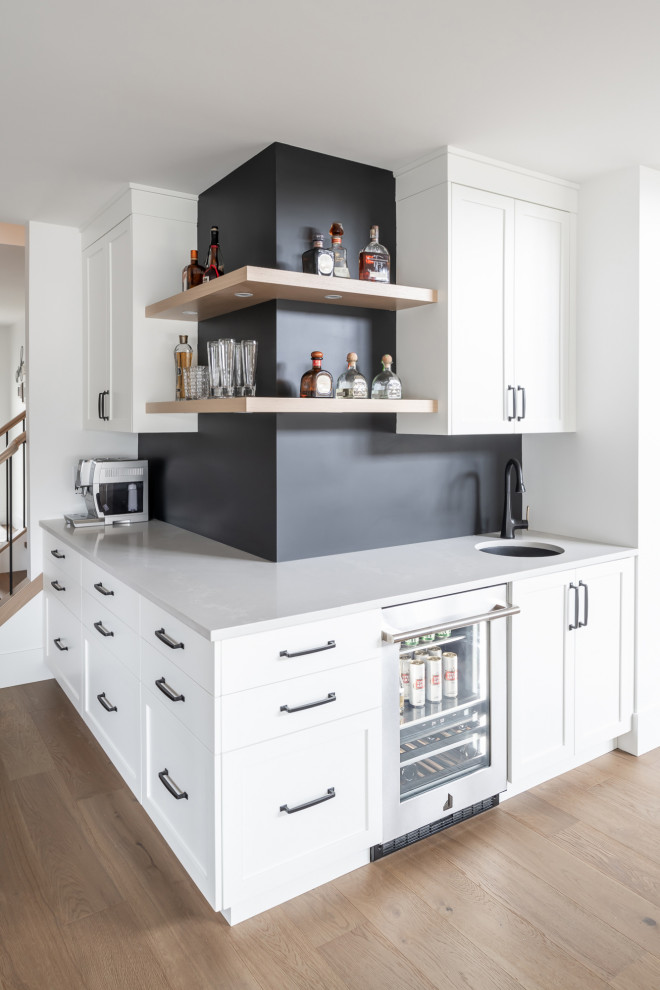 This is an example of a contemporary wet bar in Vancouver with shaker cabinets, white cabinets, quartz worktops, black splashback, medium hardwood flooring and white worktops.