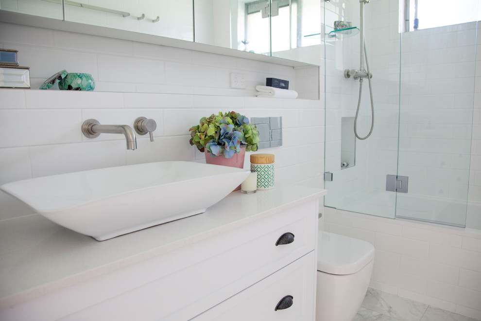 Photo of a mid-sized contemporary master bathroom in Sydney with shaker cabinets, white cabinets, a drop-in tub, a shower/bathtub combo, a wall-mount toilet, white tile, subway tile, white walls, porcelain floors, a vessel sink and engineered quartz benchtops.