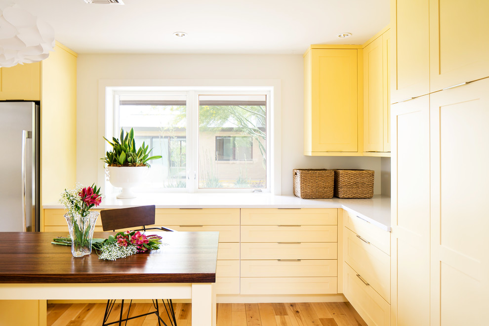 Photo of a midcentury kitchen in Phoenix with yellow cabinets, quartzite benchtops and light hardwood floors.
