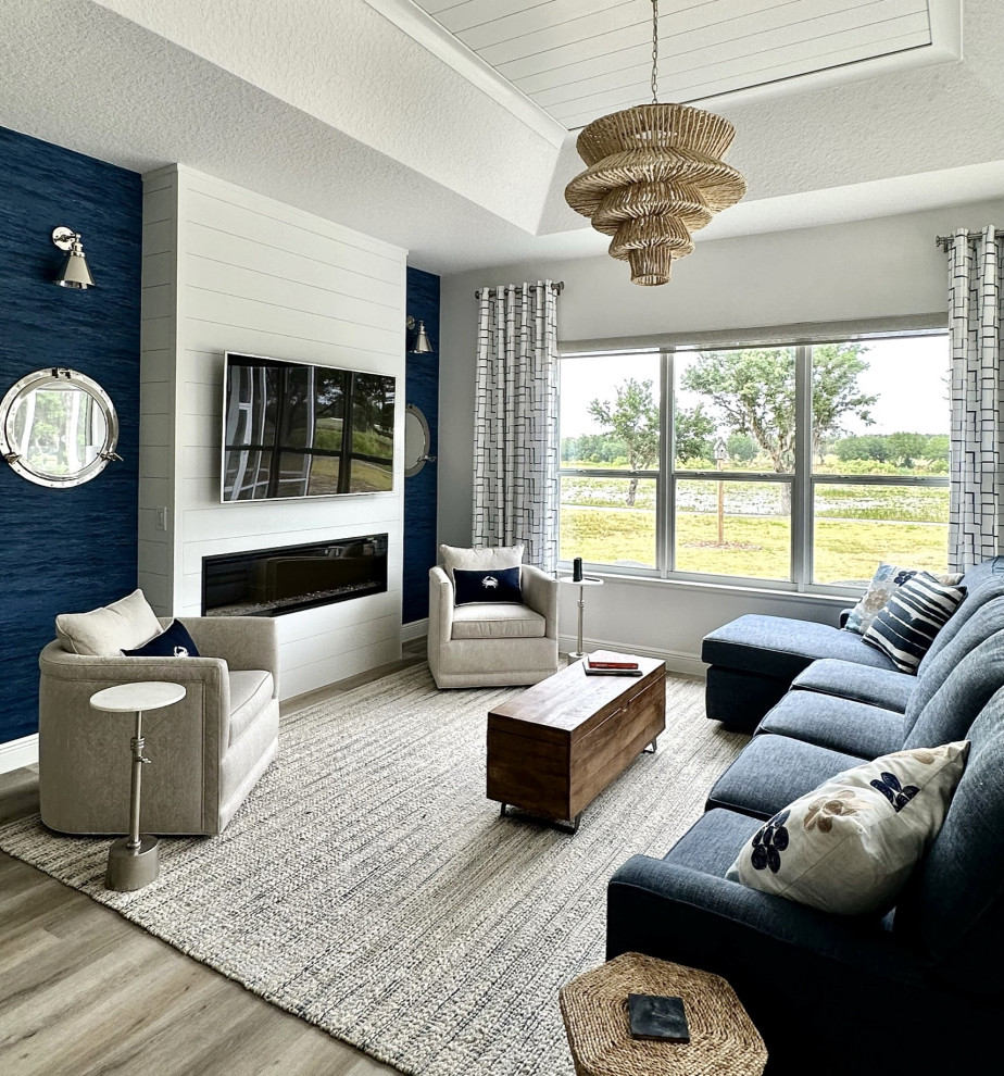 На фото: большая гостиная комната в морском стиле с синими стенами, стандартным камином, фасадом камина из вагонки, телевизором на стене, бежевым полом и потолком из вагонки