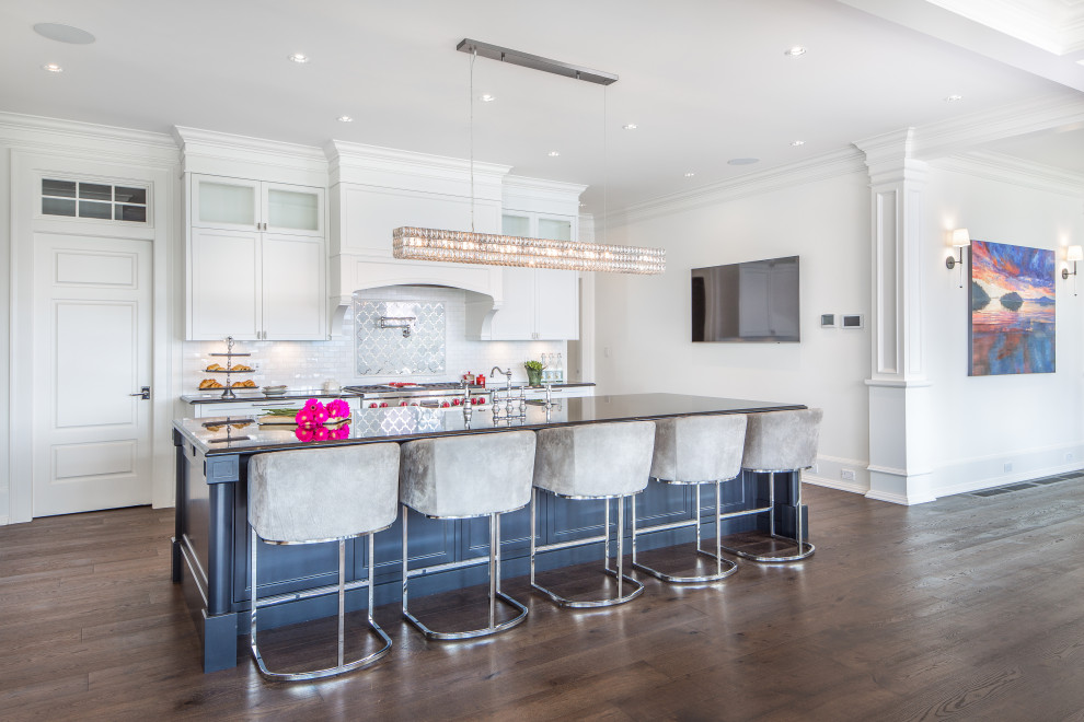 Inspiration for a transitional medium tone wood floor and brown floor kitchen remodel in Vancouver with a farmhouse sink, shaker cabinets, white cabinets, white backsplash, stainless steel appliances, an island and black countertops