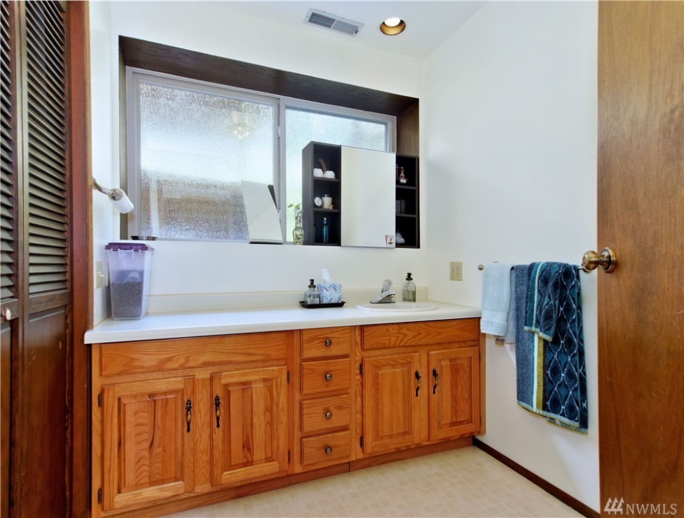 Photo of a mid-sized traditional 3/4 bathroom in Seattle with white cabinets, white walls, porcelain floors, white benchtops, a laundry and a single vanity.