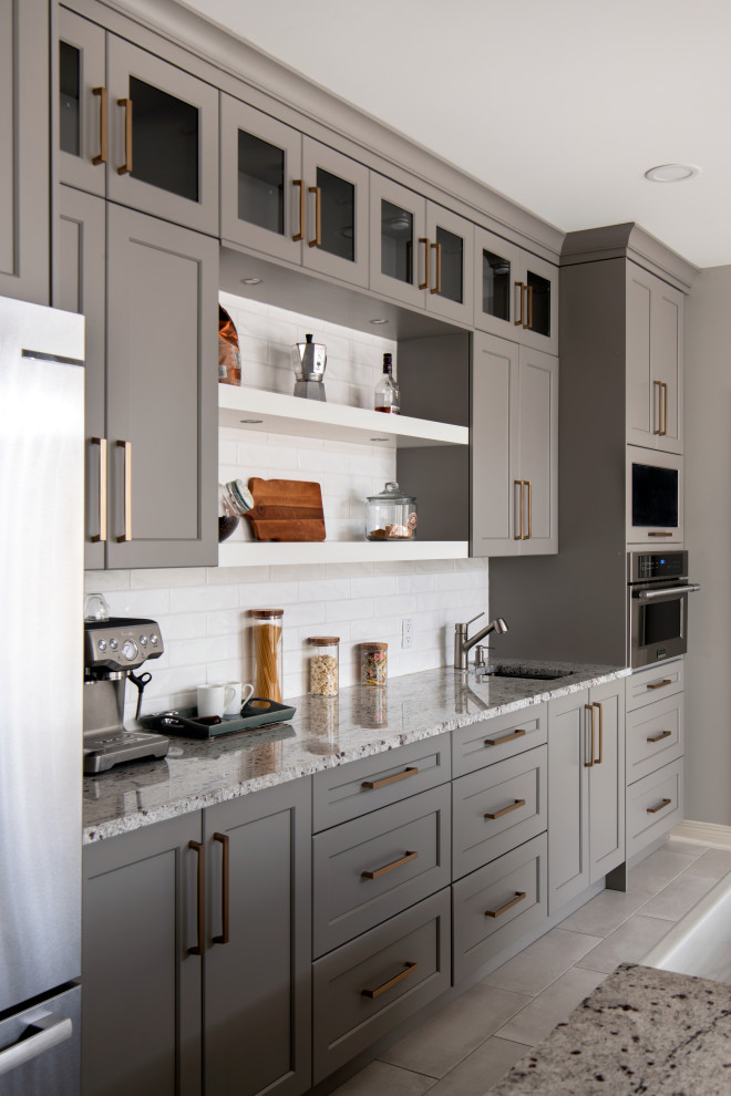 Mid-sized transitional l-shaped porcelain tile and gray floor open concept kitchen photo in Ottawa with a farmhouse sink, shaker cabinets, gray cabinets, granite countertops, white backsplash, ceramic backsplash, stainless steel appliances, an island and multicolored countertops