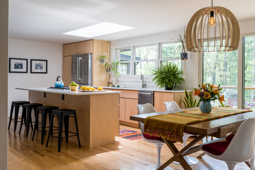 This is an example of a mid-sized eclectic galley eat-in kitchen in Indianapolis with an undermount sink, flat-panel cabinets, light wood cabinets, quartz benchtops, stainless steel appliances, medium hardwood floors, with island, brown floor and white benchtop.
