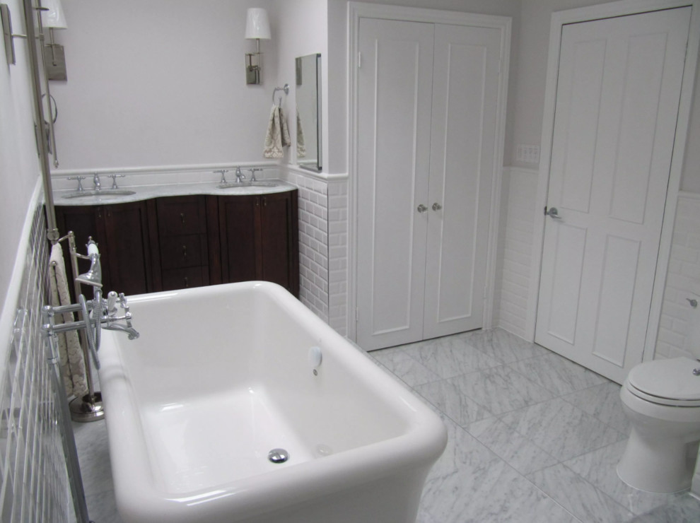 Photo of a mid-sized contemporary master bathroom in Toronto with furniture-like cabinets, brown cabinets, a freestanding tub, an open shower, a one-piece toilet, white tile, ceramic tile, grey walls, marble floors, an undermount sink, marble benchtops, grey floor, a hinged shower door and white benchtops.