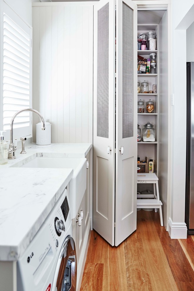 Mid-sized traditional l-shaped utility room in Sydney with a farmhouse sink, shaker cabinets, grey cabinets, white walls and medium hardwood floors.