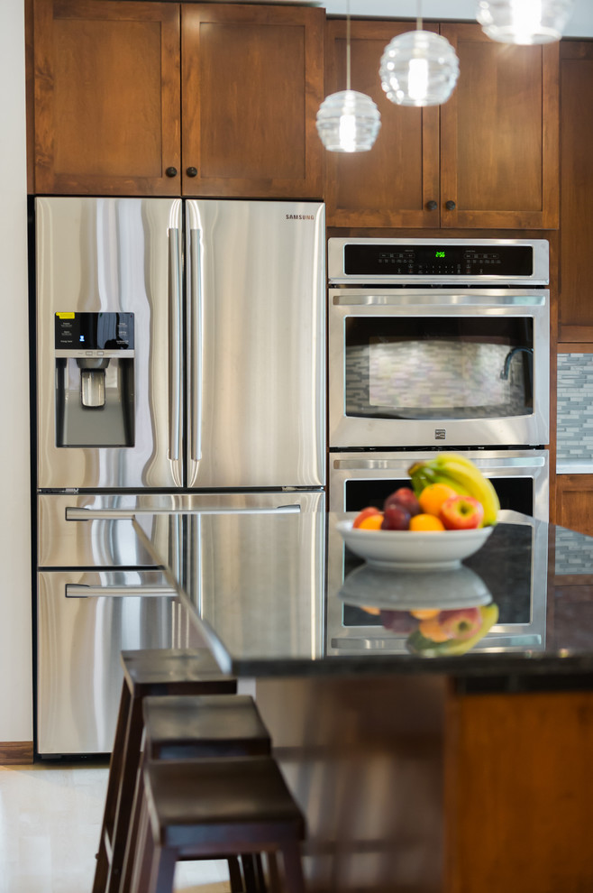 Example of a large transitional l-shaped light wood floor eat-in kitchen design with an undermount sink, shaker cabinets, dark wood cabinets, quartz countertops, gray backsplash, matchstick tile backsplash, stainless steel appliances and an island