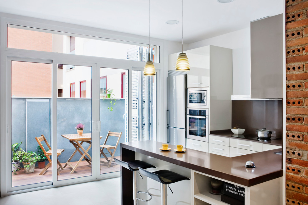 This is an example of a mid-sized contemporary u-shaped separate kitchen in Barcelona with flat-panel cabinets, white cabinets, brown splashback, stainless steel appliances, a peninsula and solid surface benchtops.