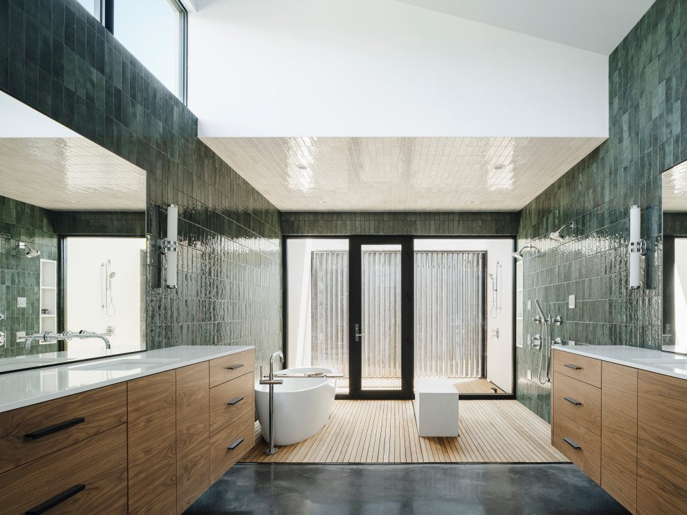 This is an example of a modern ensuite bathroom in Phoenix with flat-panel cabinets, medium wood cabinets, a freestanding bath, a walk-in shower, green tiles, ceramic tiles, a submerged sink, engineered stone worktops, white worktops, a shower bench, double sinks and a floating vanity unit.