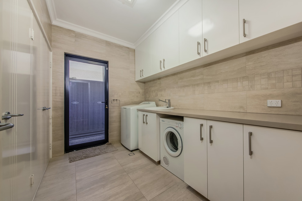 Modern galley dedicated laundry room in Perth with a single-bowl sink, flat-panel cabinets, white cabinets, quartz benchtops, beige splashback, ceramic splashback, beige walls, ceramic floors, a side-by-side washer and dryer, beige floor and grey benchtop.