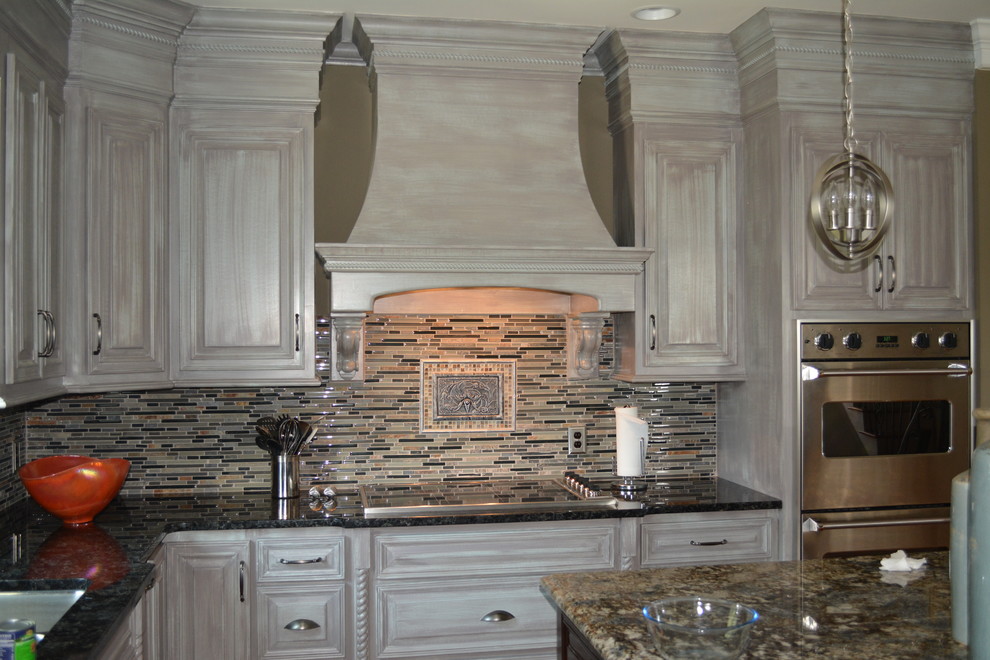 Inspiration for a mid-sized transitional l-shaped enclosed kitchen remodel with raised-panel cabinets, distressed cabinets, granite countertops, beige backsplash, matchstick tile backsplash, stainless steel appliances and an island