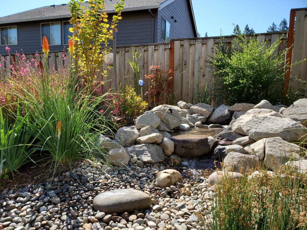 Mittelgroßer Uriger Garten im Sommer, hinter dem Haus mit Blumenbeet, direkter Sonneneinstrahlung und Flusssteinen in Portland