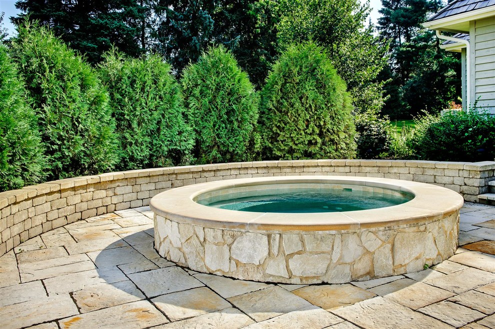 This is an example of a small traditional backyard round aboveground pool in Chicago with a hot tub and natural stone pavers.