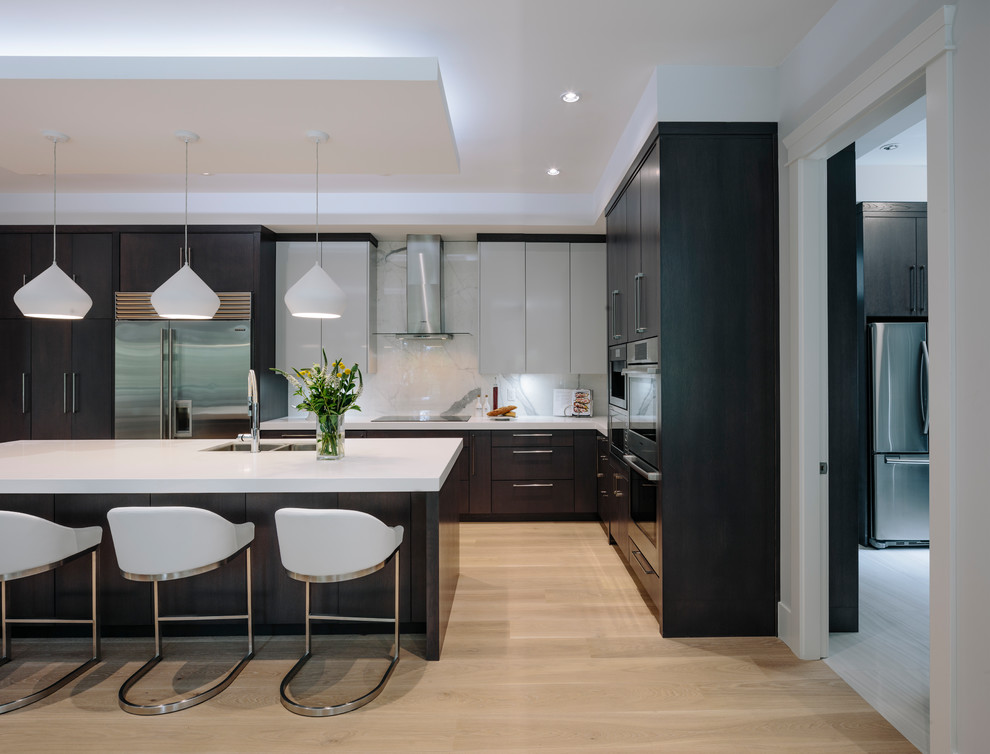 Photo of an expansive modern l-shaped open plan kitchen in Vancouver with an undermount sink, flat-panel cabinets, dark wood cabinets, quartz benchtops, white splashback, marble splashback, stainless steel appliances, light hardwood floors, with island and brown floor.