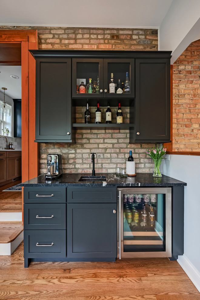 Inspiration for a transitional single-wall medium tone wood floor and brown floor wet bar remodel in Chicago with an undermount sink, shaker cabinets, black cabinets, brick backsplash and black countertops