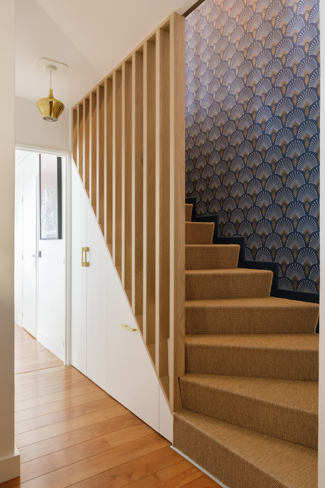 Cette image montre un escalier courbe design de taille moyenne avec des marches en moquette, des contremarches en moquette, un garde-corps en bois, du papier peint et rangements.