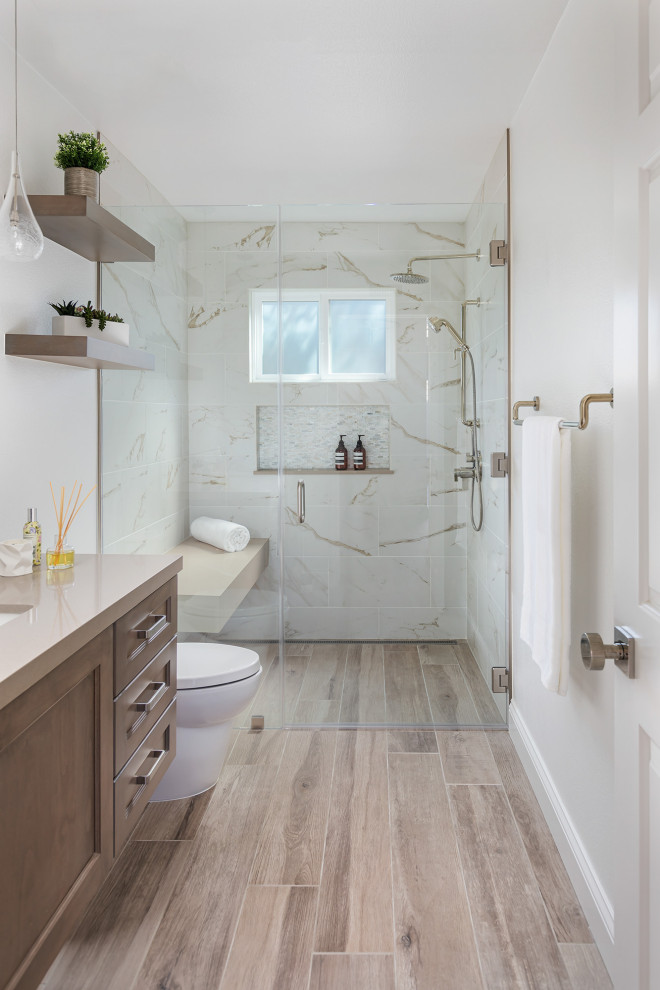 This is an example of a transitional 3/4 bathroom in Orange County with medium wood cabinets, a curbless shower, multi-coloured tile, white walls, wood-look tile, an undermount sink, brown floor, a hinged shower door, beige benchtops, a niche, a shower seat, a single vanity, a built-in vanity and recessed-panel cabinets.