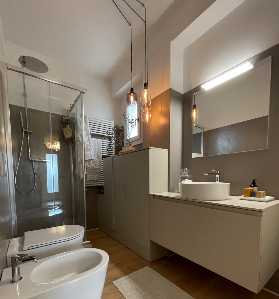 Пример оригинального дизайна: ванная комната среднего размера в стиле модернизм с плоскими фасадами, серыми фасадами, угловым душем, биде, серой плиткой, серыми стенами, паркетным полом среднего тона, душевой кабиной, настольной раковиной, столешницей из ламината, бежевым полом, душем с раздвижными дверями, бежевой столешницей, зеркалом с подсветкой, тумбой под одну раковину и подвесной тумбой