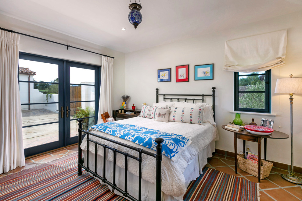 Design ideas for a mid-sized mediterranean guest bedroom in San Luis Obispo with white walls, terra-cotta floors and brown floor.