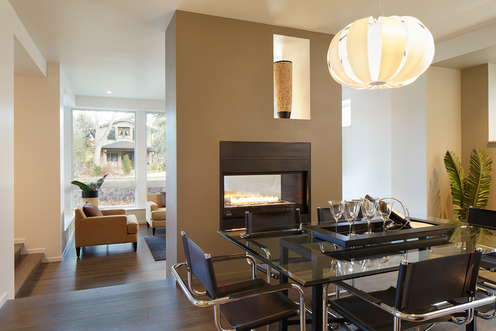 Inspiration for a mid-sized contemporary open plan dining in Denver with a two-sided fireplace, beige walls, dark hardwood floors, a metal fireplace surround and brown floor.