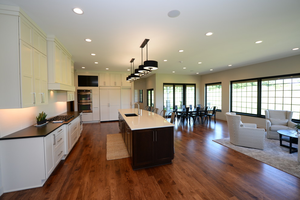 Inspiration for a large transitional single-wall medium tone wood floor open concept kitchen remodel with an undermount sink, recessed-panel cabinets, white cabinets, granite countertops, white backsplash, stainless steel appliances and an island