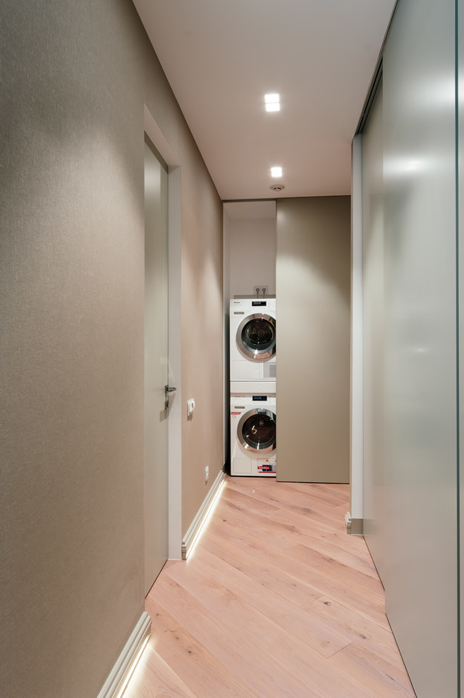 This is an example of a mid-sized contemporary laundry cupboard in Moscow with beige walls, light hardwood floors and a stacked washer and dryer.