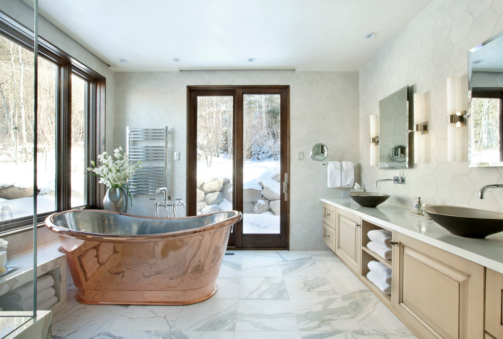 Inspiration for an expansive country master bathroom in Denver with raised-panel cabinets, beige cabinets, a freestanding tub, stone tile, marble floors, a vessel sink, marble benchtops and beige tile.