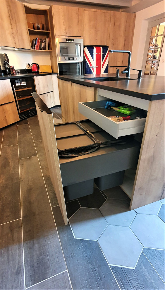 Design ideas for a large contemporary l-shaped open plan kitchen in Other with an integrated sink, flat-panel cabinets, light wood cabinets, granite benchtops, black splashback, granite splashback, panelled appliances, cement tiles, with island, grey floor, black benchtop and exposed beam.