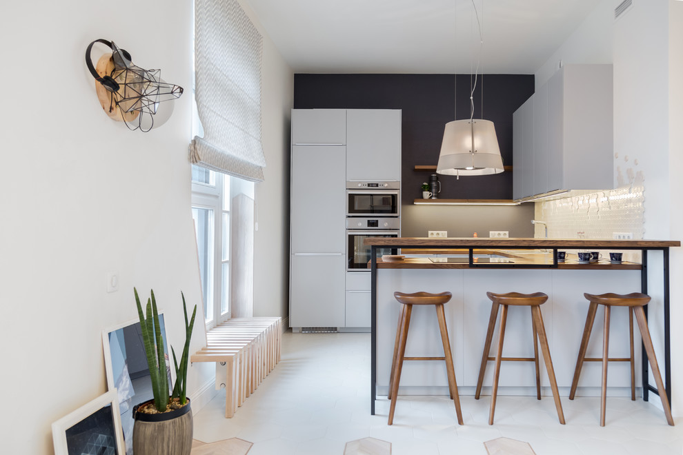 Photo of a small scandinavian u-shaped open plan kitchen in Saint Petersburg with a drop-in sink, flat-panel cabinets, grey cabinets, wood benchtops, beige splashback, mosaic tile splashback, stainless steel appliances, ceramic floors, a peninsula and beige floor.
