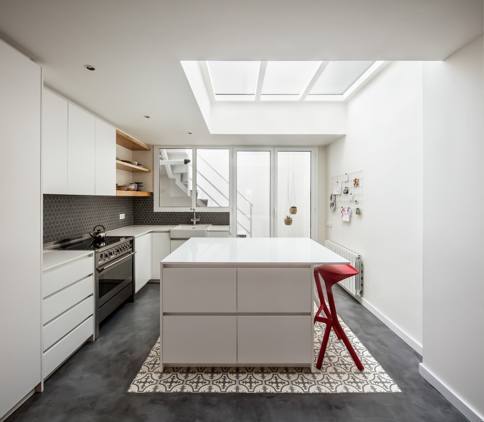 Photo of a contemporary l-shaped separate kitchen in Barcelona with a drop-in sink, flat-panel cabinets, white cabinets, black splashback, mosaic tile splashback, panelled appliances, concrete floors, with island, grey floor and white benchtop.
