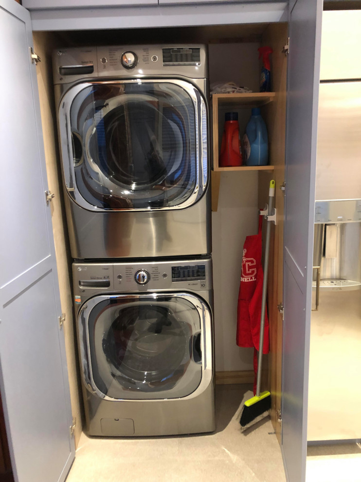 Small traditional laundry cupboard in New York with shaker cabinets, blue cabinets, quartz benchtops, white splashback, engineered quartz splashback, red walls, travertine floors, a stacked washer and dryer, beige floor and white benchtop.